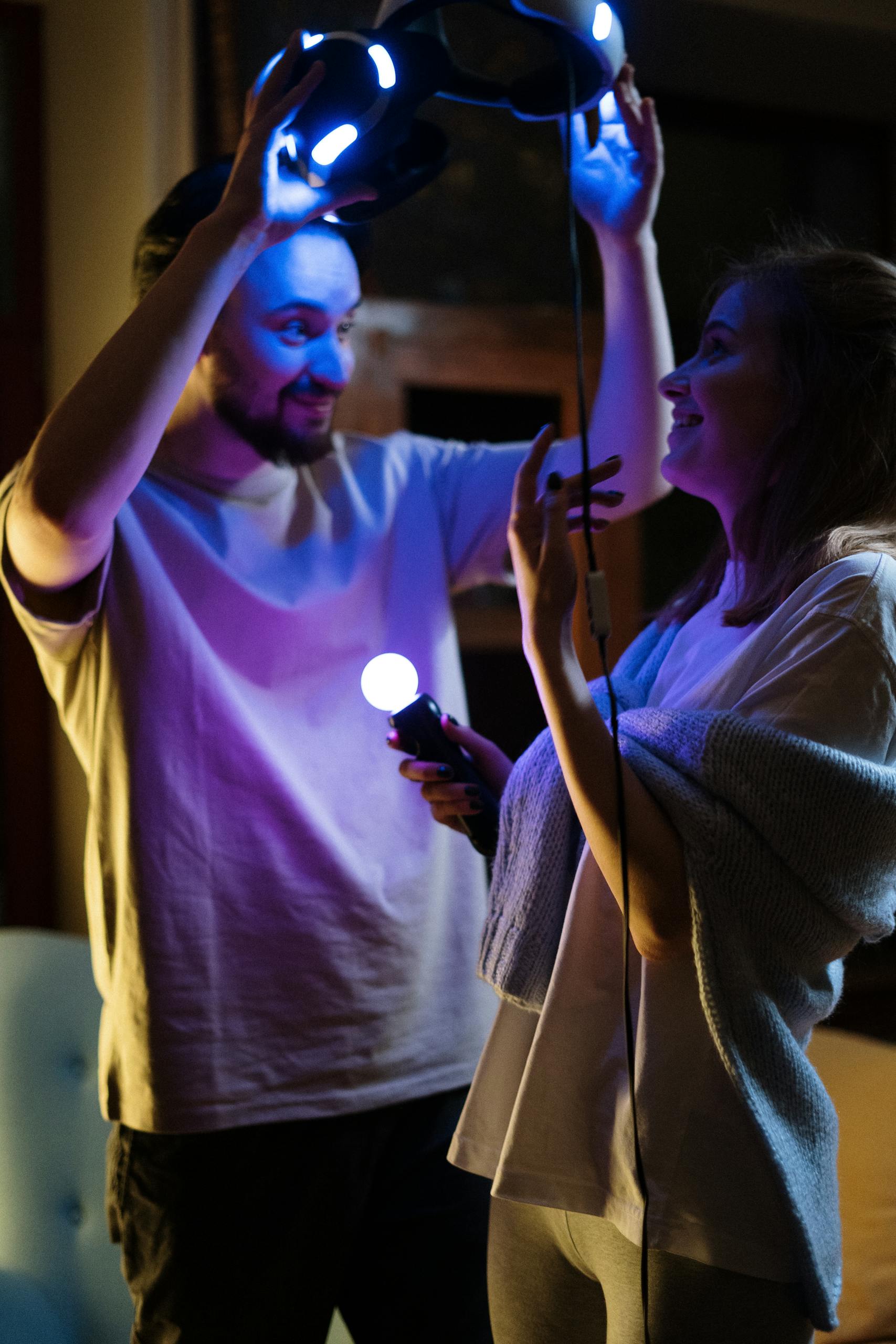 A joyful couple plays with a virtual reality headset in a cozy home setting during the evening.